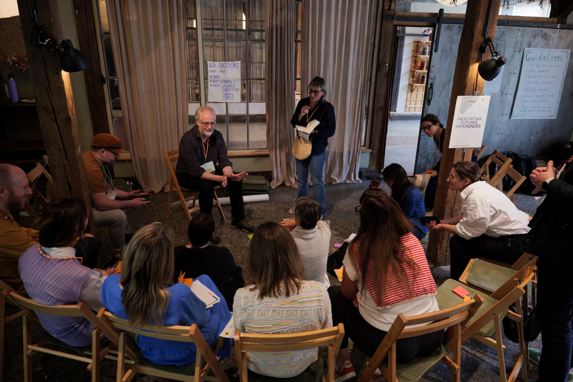 A group seated in a circle inside a rustic indoor space with wooden columns